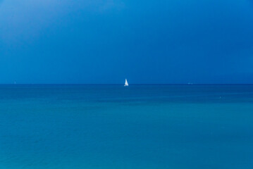 Fototapeta premium Minimalist seascape with a small white sailboat on a deep blue horizon