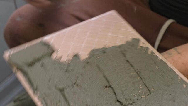 Tile adhesive spreading. Tiling mortar application. Worker smoothing adhesive. Workman smoothing grout on ceramic tiles. Bathroom renovation. Man using notched trowel, cement spread across tile back
