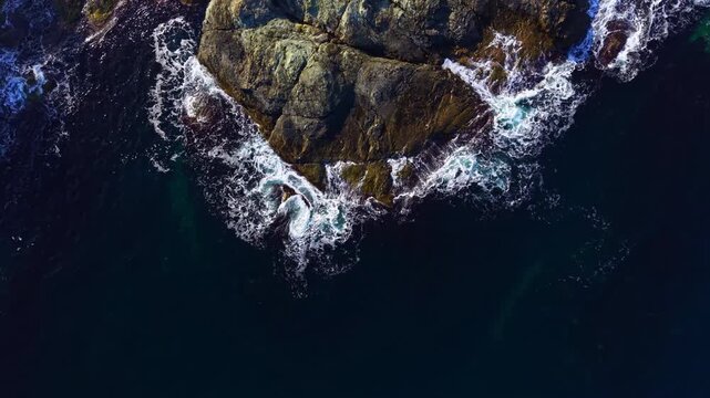 Surging waves collide with rocky formations at twilight, casting reflections of golden light on the water's surface, showcasing nature's raw beauty along a secluded coast.