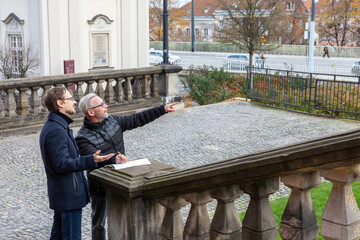 Two people discuss plans near a historic building on a clear day in a city