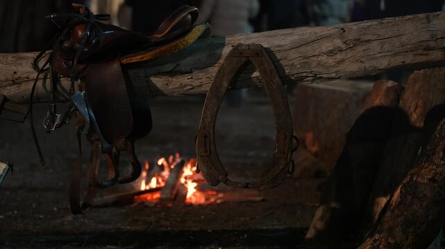 Horse Saddle and Bridle Equipment Resting on Tree Stump Near a Glowing Travelers Campfire Outdoors