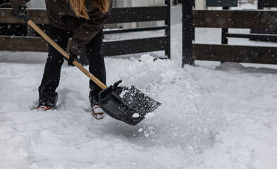 Young woman with a snow shovel clears snow from the sidewalk in front of her house