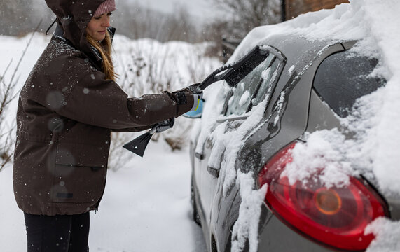 Woman clears snow from her car after a heavy snowfall using a snow brush