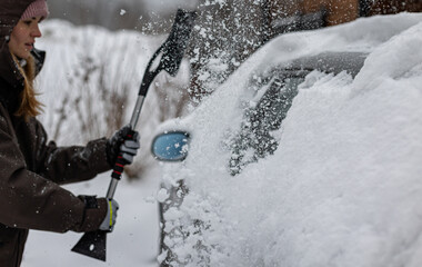 Woman clears snow from her car after a heavy snowfall using a snow brush