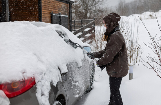 Woman clears snow from her car after a heavy snowfall using a snow brush