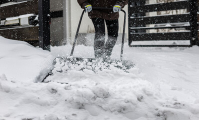 Large snow shovel in the hands of a woman clearing snow from her backyard