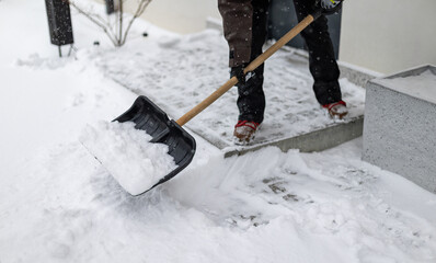 Snow shovel in the hands of a woman clearing snow from a snow-covered entrance to a house