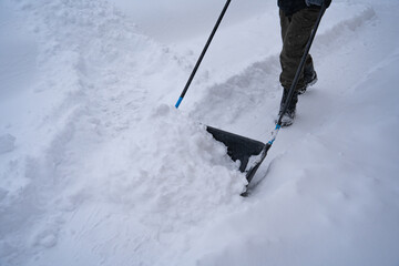 A man in a dark jacket shovels snow near a house, a village street, winter, snowdrifts