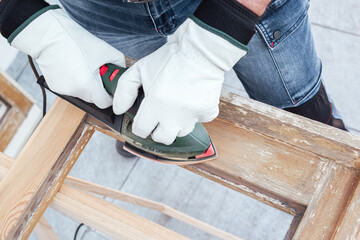 View from above. Adult carpenter using an electric sander to smooth an old wooden window. Construction industry, carpentry, housework do it yourself, workplace safety. Restoration.