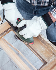 View from above. Adult carpenter using an electric sander to smooth an old wooden window. Construction industry, carpentry, housework do it yourself, workplace safety. Restoration.