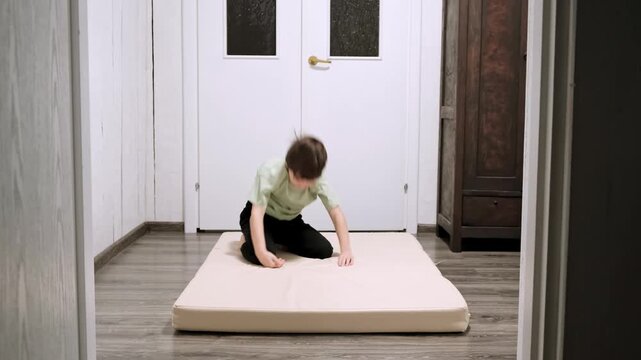 Caucasian boy doing somersaults back and forth on sports mat in home interior. Children workout. Happy child strengthening the muscles. Strong body. Kid does sports exercise. High quality 4k footage.