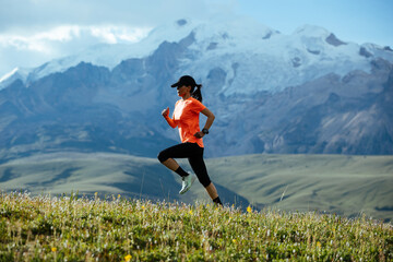 Woman runner running on the beautiful flowering grassland mountain top