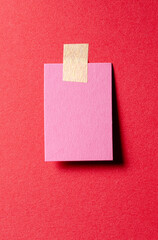 Piece of pink paper note with adhesive sticky tape and shadow on red background
