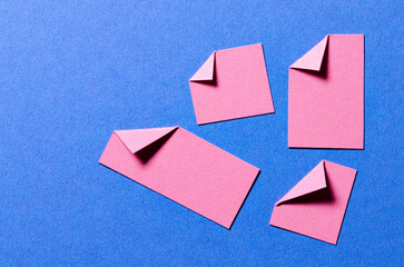 Pink paper message notes or sheets with folded edge dog-ear earmark and copy space for text on blue background, top view flat lay desk backdrop