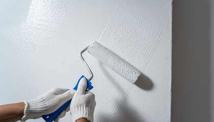 白い壁をローラーで塗装する職人の手元アップ