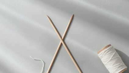 Wooden knitting needles and a cotton bobbin placed in a corner on a gray backdrop, used for layout design in hobby supplies, March 2024
