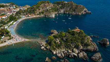 Obraz premium Aerial view of Isola Bella in Taormina, Sicily, Italy. The island is connected to the mainland by a narrow pebble beach, surrounded by a crescent-shaped bay with vibrant turquoise and deep blue water.