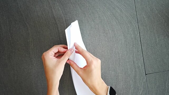 Top view close up of woman hands folding paper airplane on desk in home office. Playful break, creative thinking pause and mental reset within everyday work routine in real life workspace