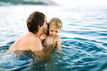 Father and baby boy swimming together in the sea, family bonding, summer vacation, love and parenthood.
