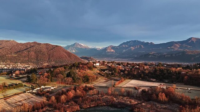 Aerial drone shot pulling back to reveal a frozen lake surrounded by winter countryside and distant mountains, calm and cinematic landscape at sunrise.