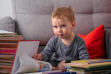 Cheerful toddler reading books on sofa, illustrating early learning habits, literacy development, curiosity, and happy childhood moments at home.