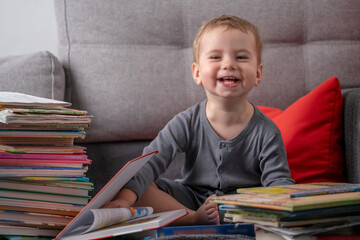 Happy toddler sitting on sofa surrounded by colorful books, smiling with joy, symbolizing early learning, curiosity, childhood happiness, and love for reading at home.