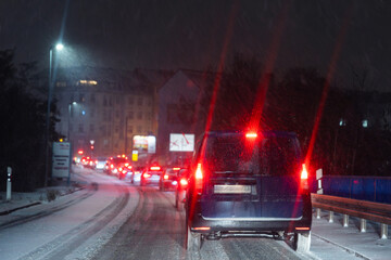 Winter traffic jam on snowy urban road night with long queue cars, glowing red taillights, icy asphalt, falling snow, poor visibility and stressful commute conditions. Cold city transport atmosphere