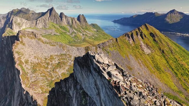 Man standing on the summit of Segla mountain on Senja Island, Norway, dramatic Nordic landscape with steep peaks and fjords, moment of achievement, freedom and wild nature. Aerial View
