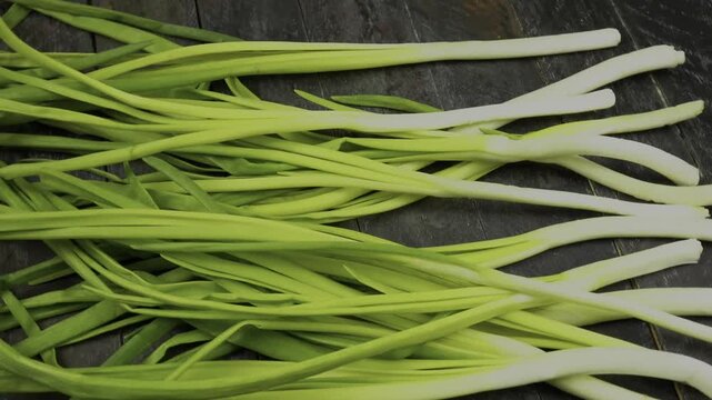 Bundle of scallion lying on a wooden board, rotation, top view. Ingredient for preparing vegetable dishes.