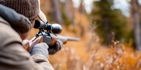 Hunter aiming a scoped rifle in an autumn forest.