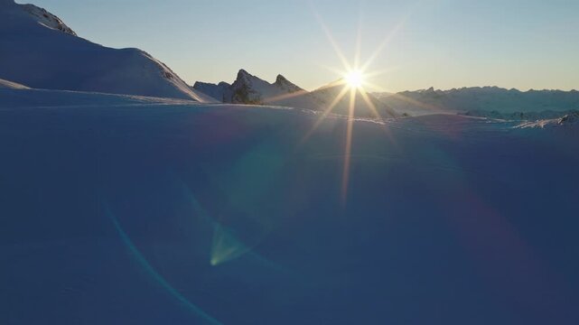 Aerial footage of snowy alpine peaks in Austria during sunset. Warm golden light reflecting off white mountain summits creates a breathtaking winter landscape captured in cinematic 4K.