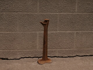 Old rusty metal stand or support standing on concrete near gray wall, vertical shape, rough texture.
