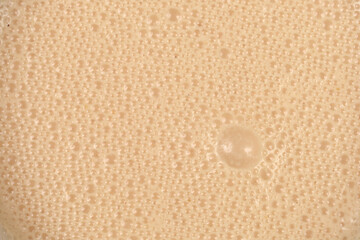 A top down macro view of a creamy beige beverage surface covered in a dense layer of tiny bubbles and organic foam patterns