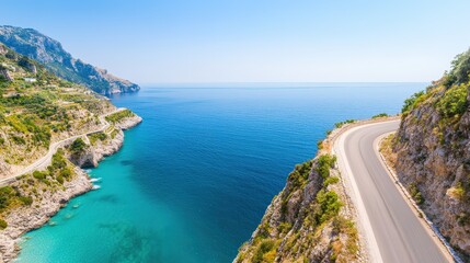 A scenic coastal road curves along rocky cliffs overlooking crystal-clear blue sea under a bright, sunny sky.