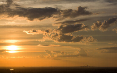 Obraz premium The sun sets behind a vast landscape with a predominantly orange sky filled with scattered clouds during a serene moment of natural beauty at dusk