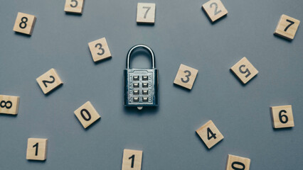 Silver combination padlock surrounded by scattered wooden number tiles on a gray background for cybersecurity concept