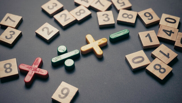 Primary math operation signs with scattered wooden numbers on gray textured surface for educational and problem solving themes