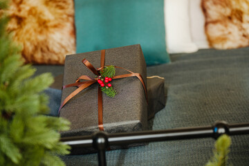 Dark gift box tied with ribbon and berries near green pine branch and soft pillows