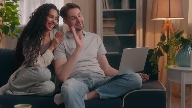 Multiethnic couple at home with Caucasian man and Hispanic woman making video call on laptop cheerful married spouses talking virtual conference chat conversation saying goodbye waving hands indoors