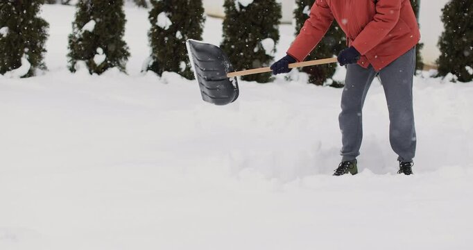 Young man cleans snow with a shovel after snowfall background of the house in winter.