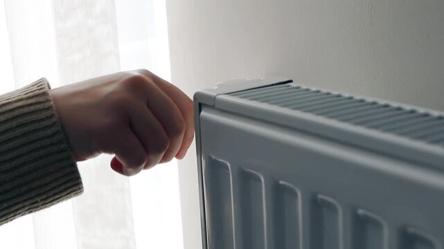 Regulation control of the heating temperature on the battery in the room, female hand. Adjusting turn on heating up, thermostatic radiator valve on radiator.