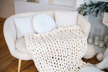 Fototapeta premium Cozy cream sofa with knit blanket and pillows, warm winter home interior scene.