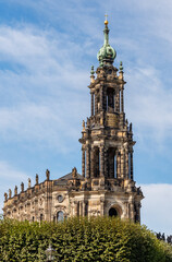Magnificent baroque cathedral tower featuring ornate stone sculptures and a green copper dome. Historic architecture against a soft blue sky