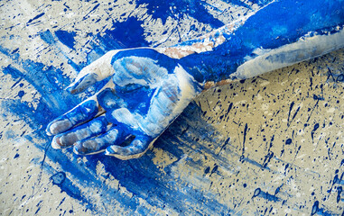 Paint covered human hand resting on abstract blue splattered surface, expressive body art detail symbolizing creativity, touch, process and raw artistic action in contemporary art
