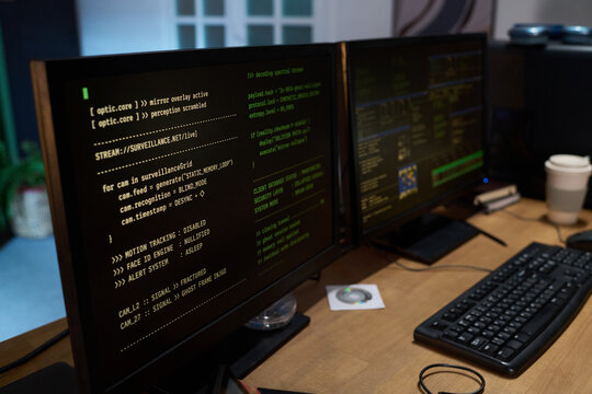 Dual computer monitors displaying surveillance camera code and system logs on wooden desk, showing close up of programming interface with coffee cup and compact disc nearby - Powered by Adobe