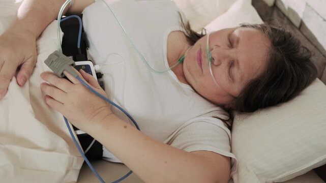 Woman wearing portable sleep tracker on abdomen, Female patient with sleep and health monitoring device on abdomen and fingertip pulse oximeter for continuous tracking