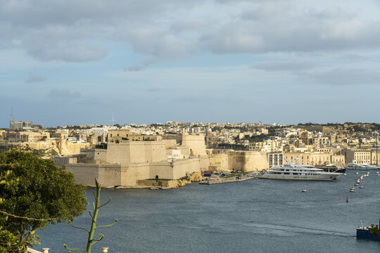 View of sunlight kissing the ancient fort st angelo walls as yachts glide on the tranquil waters of the harbor, Valletta, Malta.