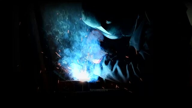 A welder at work. Welding of metal parts. A high-temperature process that involves joining two or more metal parts by fusing them.