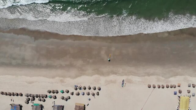 A drone shot of a beach in Goa with calm sea waves and beach umbrellas and shacks from bird eye view.