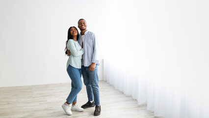 Real estate concept. Happy african american couple embracing and standing in empty white room of their new apartment, panorama with empty space for advertisement